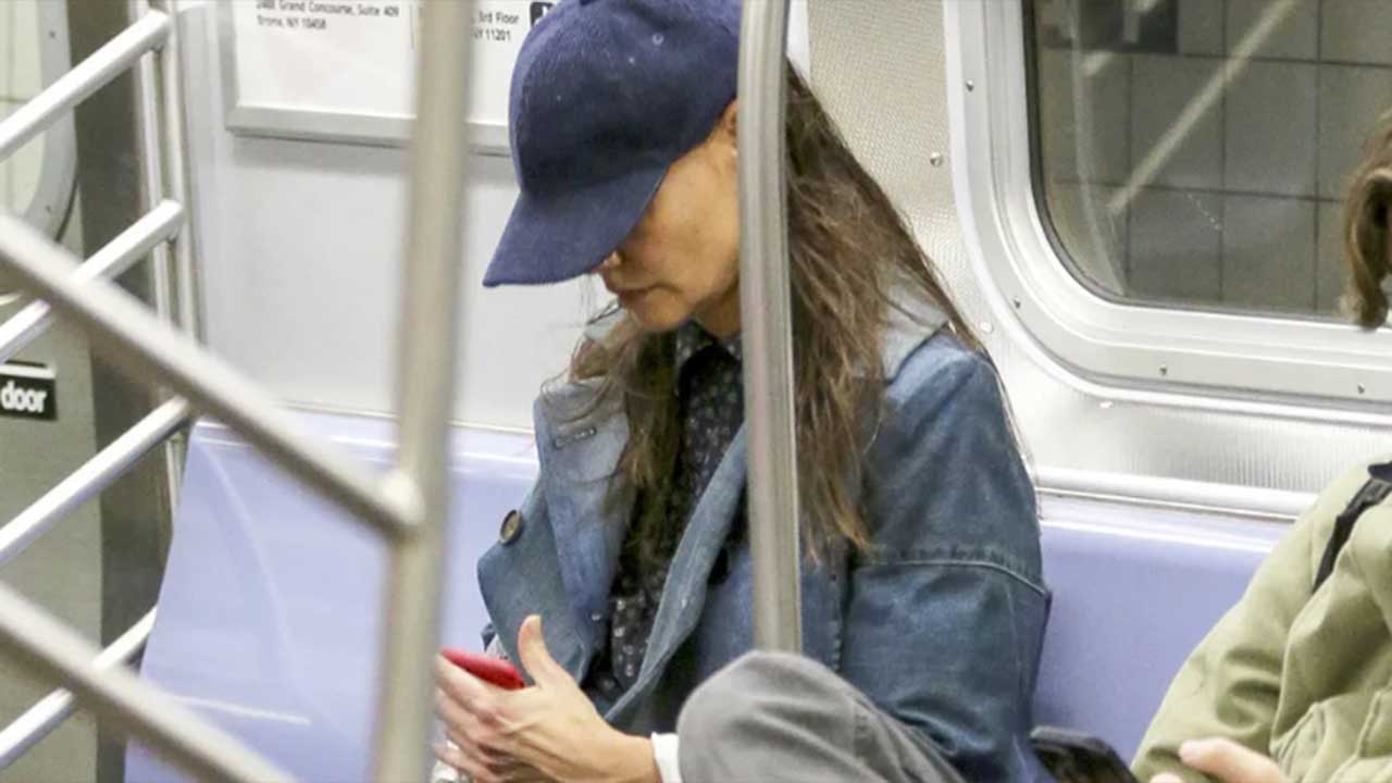 Atriz famosa Kate Holmes sentada no metrô mexendo no celular